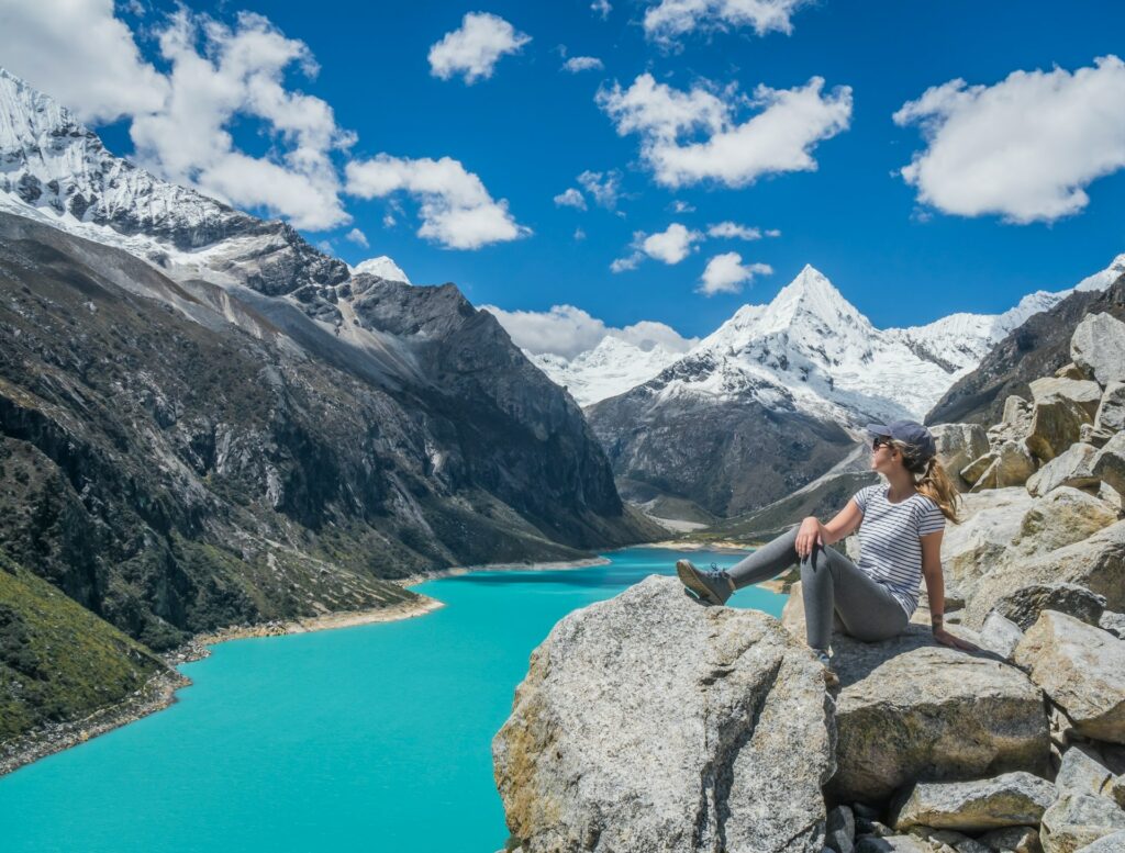 Woman Perched Atop a Rugged Rock Overlooking a Tranquil Lake In Daylight